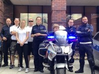 policjanci pozują do zdjęcia na tle motocykla i radiowozów policyjnych