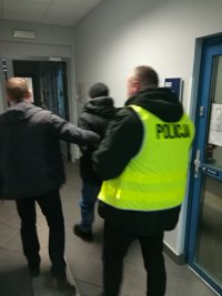 zdjęcie kolorowe, przedstawia policjantów z zatrzymanym