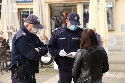 dwóch policjantów w maseczkach legitymuje kobietę