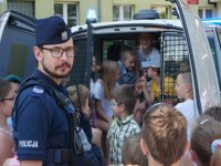 zdjęcie kolorowe na zdjęciu widać policjanta oraz dzieci siedzące w radiowozie