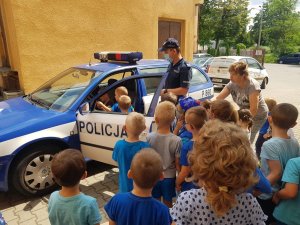 Umundurowany policjant w masce pokazuje dzieciom radiowóz