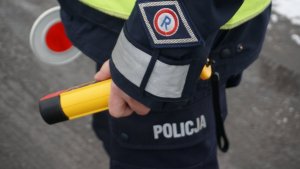 Policjant w ręku trzyma tarczę do zatrzymywania pojazdów oraz urządzenie do sprawdzania stanu trzeźwości