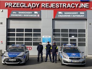 Policjanci stoją przy radiowozach na tle stacji diagnostycznej