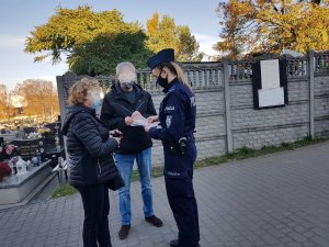 Umundurowana policjantka wręcza kobiecie i mężczyźnie ulotki