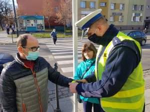 Policjant zakłada na rękę mężczyzny opaskę odblaskową