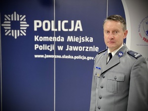 Policjant a za nim ścianka z napisem Komenda Miejska Policji w Jaworznie