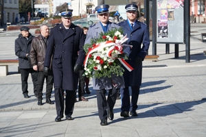 Na pierwszym planie funkcjonariusz w umundurowaniu galowym niosący wieniec, za nim Komendant Komendy Miejskiej Policji w Jaworznie oraz Komendant Państwowej Straży Pożarnej w Jaworznie