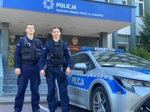 Policjanci stoją przed komendą przy radiowozie