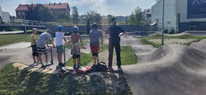 Policjantka razem z młodzieżą na hulajnogach, w tle pumptrack