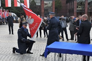 Zdjęcie. Moment przekazania i wręczania sztandaru. Widoczni umundurowani policjanci oraz poczty sztandarowe.