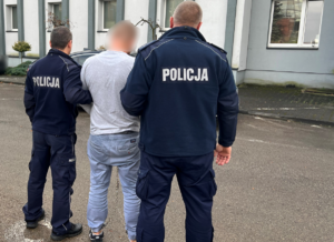 Policjanci stoją przed komendą z zatrzymanym