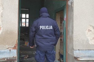 na zdjęciu policjant w mundurze stojący w drzwiach pustostanu