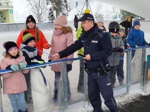 na zdjęciu grupa dzieci stojąca na lodowisku oraz umundurowany policjant