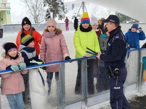 na zdjęciu grupa dzieci stojąca na lodowisku oraz umundurowany policjant