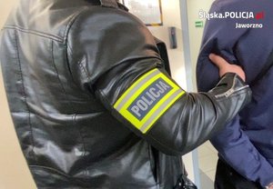 na zdjęciu mężczyzna z opaską na ramieniu z napisem Policja trzymający za ramię zatrzymanego