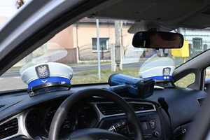 na zdjęciu dwie czapki policyjne z ruchu drogowego leżące na desce rozdzielczej w radiowozie