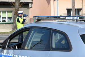 na zdjęciu umundurowany policjant dokonujący pomiaru prędkości, w tle radiowóz policyjny