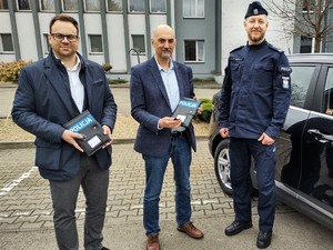 na zdjęciu umundurowany policjant oraz dwóch przedstawicieli władz miasta trzymających karty do pojazdów