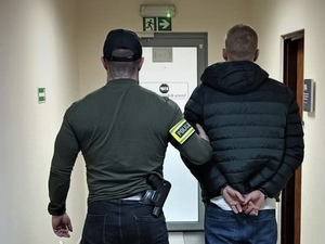 na zdjęciu nieumundurowany policjant, który trzyma zatrzymanego na korytarzu