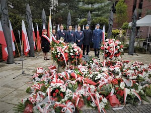 na zdjęciu przedstawiciele władz miasta oraz komendant miejski policji w Jaworznie stojący pod pomnikiem niepodległości, na ziemi, pod pomnikiem leży duża ilość wieńców z kwiatów
