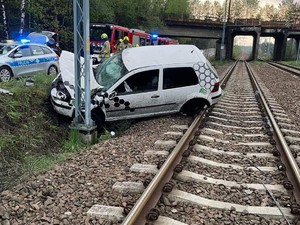 na zdjęciu uszkodzony samochód osobowy, który uderzył w słup trakcyjny znajdujący się na torach kolejowych. Z lewej strony radiowozy służb ratowniczych.