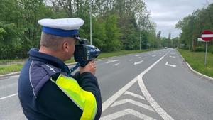 na zdjęciu policjant w mundurze, który przy jezdni dokonuje pomiaru prędkości