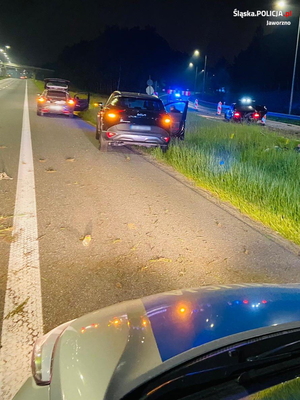 na zdjęciu roztrzaskany samochód stojący na autostradzie w kolorze czarnym, z którego się dymi