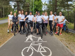 na zdjęciu grupa osób stojąca przy rowerach, osoby na rolkach. Na przodzie grupy stoi umundurowany patrol rowerowy.