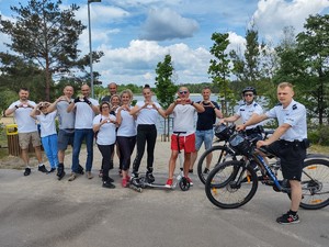 na zdjęciu grupa osób, która pokazuje rękoma znak serce. Po prawej stronie umundurowany rowerowy patrol policji.