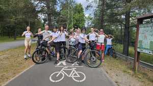 na zdjęciu grupa osób stojąca przy rowerach, na rolach i jedna osoba na hulajnodze. Osoby rękoma tworzą znak serce. Na przodzie grupy dwuosobowy patrol rowerowy policjantów