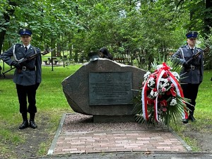 na zdjęciu dwóch umundurowanych policjantów stojących przy pomniku. Obok pomnika stoi wieniec kwiatów.