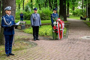 na zdjęciu trzech umundurowanych policjantów. Jeden z nich trzyma wieniec z kwiatami.