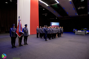 pododdział policjantów stojących w szyku na hali, obok nich stoją policjanci z pocztem sztandarowym