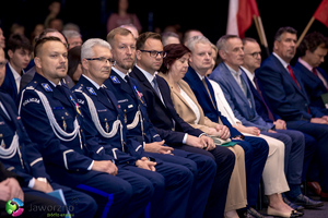 na zdjęciu umundurowani policjanci siedzący na krzesłach w hali oraz zaproszeni goście