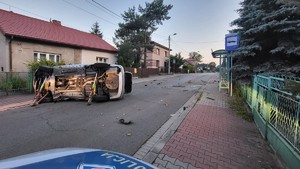 na zdjęciu samochód leżący na boku na ulicy, wokół pojazdu roztrzaskane elementy karoserii, przód radiowozu policyjnego