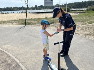 na zdjęciu umundurowana policjantka, która zakłada dziecku opaskę odblaskową