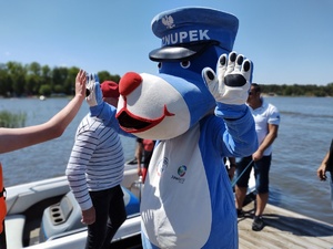 na zdjęciu policyjna maskotka Sznupek, który przybija piątkę innej osobie.