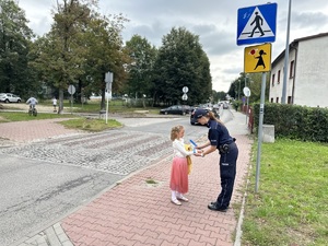 umundurowana policjantka wręcza dziewczynce opaskę odblaskową na rękę przy przejściu dla pieszych