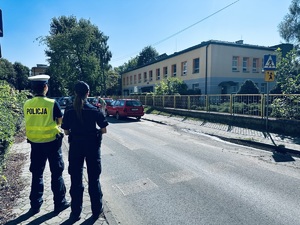 dwóch umundurowanych policjantów obserwuje przejście dla pieszych przy przedszkolu