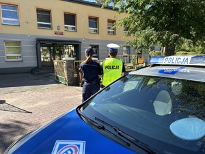 dwóch umundurowanych policjantów obserwuje przedszkole przy radiowozie