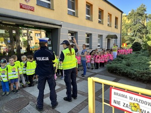 dwóch umundurowanych policjantów prowadzi prelekcję dla przedszkolaków przed przedszkolem