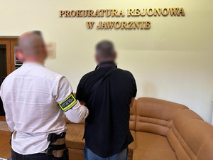 na zdjęciu nieumundurowany policjant trzyma zatrzymanego w budynku prokuratury