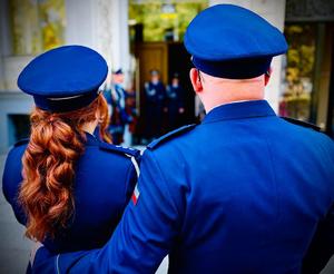 na zdjęciu dwóch umundurowanych policjantów stojących na wprost urzędu stanu cywilnego. Policjant obejmuje policjantkę