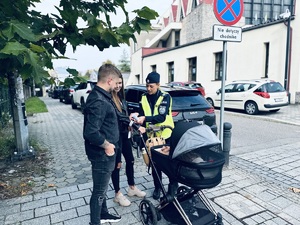 na zdjęciu policjantka wręcza opaski odblaskowe mężczyźnie i kobiecie z wózkiem