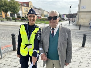 na zdjęciu umundurowana policjantka oraz starszy mężczyzna. Oboje pokazują opaski odblaskowe na rękach