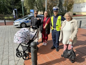 na zdjęciu grupa kobiet z umundurowanym policjantem. Kobiety pokazują, iż otrzymały od policjanta opaski odblaskowe, w tle radiowóz policyjny