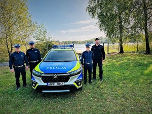 na zdjęciu czterech umundurowanych policjantów stoi przy radiowozie oznakowanym