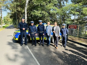 na zdjęciu umundurowani policjanci oraz przedstawiciele władz miasta, stojący przy oznakowanym radiowozie policyjnym