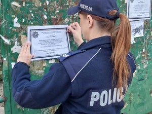 na zdjęciu umundurowana policjantka nakleja klepsydrę na tablicę ogłoszeń