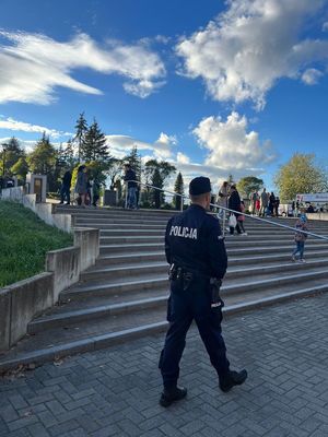 na zdjęciu umundurowany policjant idzie chodnikiem przy cmentarzu